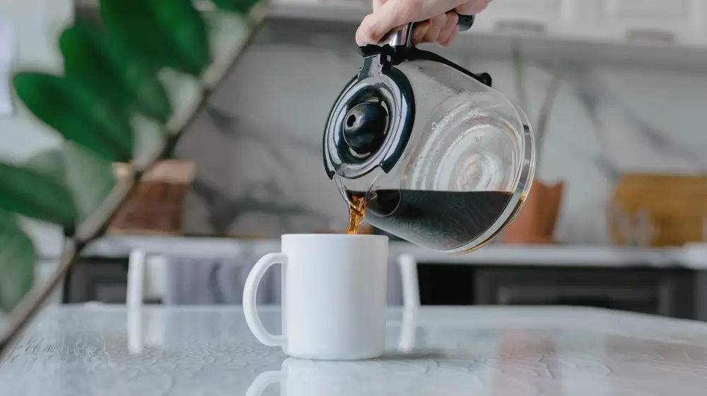 a woman pouring decaf coffee in a white cup on the kitchen counter