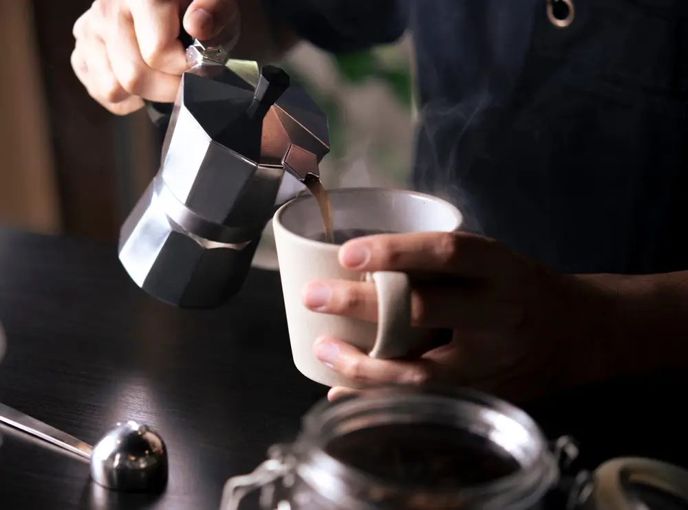 barista pouring a cup of black coffee from a steel kettle